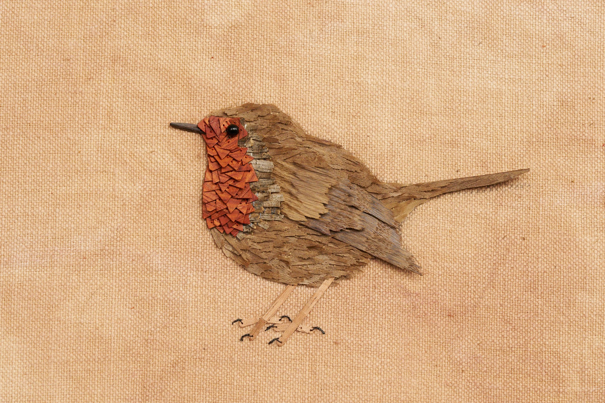 Un oiseau brodé en bois, fil et paillettes sur une toile de lin